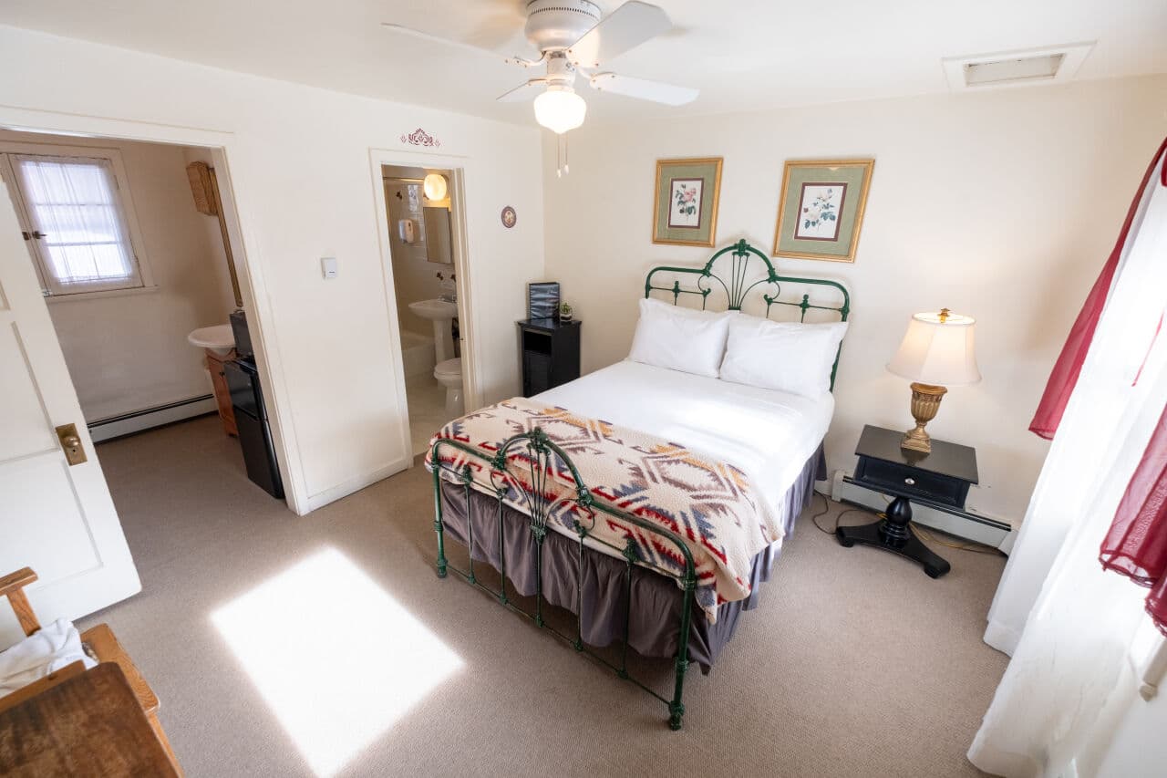 A cozy bedroom featuring a green metal bed frame, warm blankets, and a bedside table with a lamp.