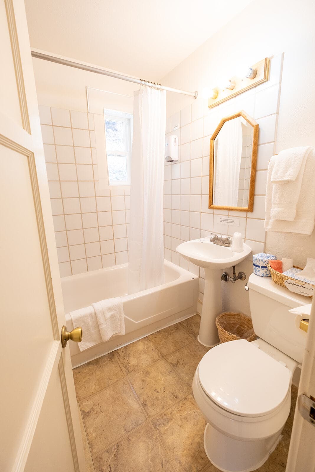 A clean, well-lit bathroom featuring a bathtub, sink, and toilet with tile walls and natural light.