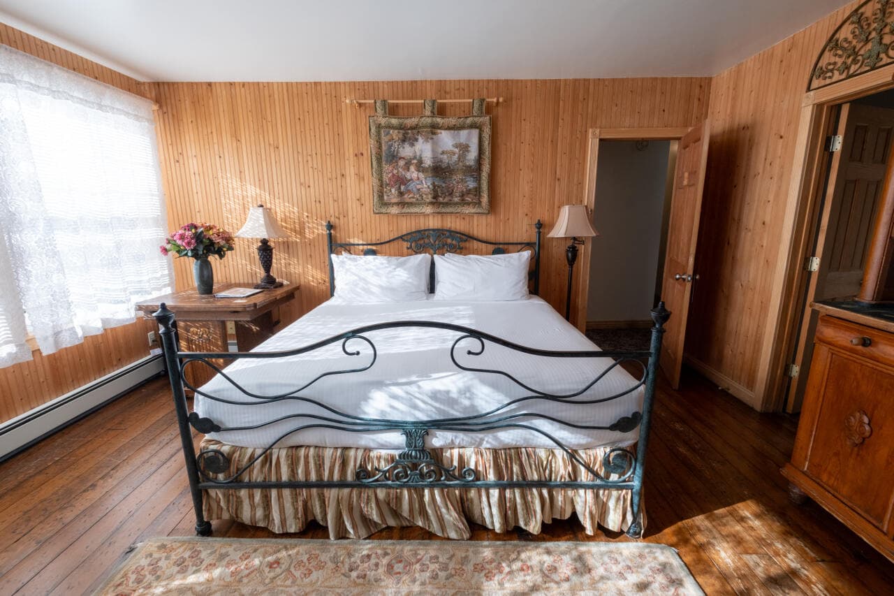 A cozy bedroom featuring a wrought iron bed, wooden walls, and natural light from a large window.