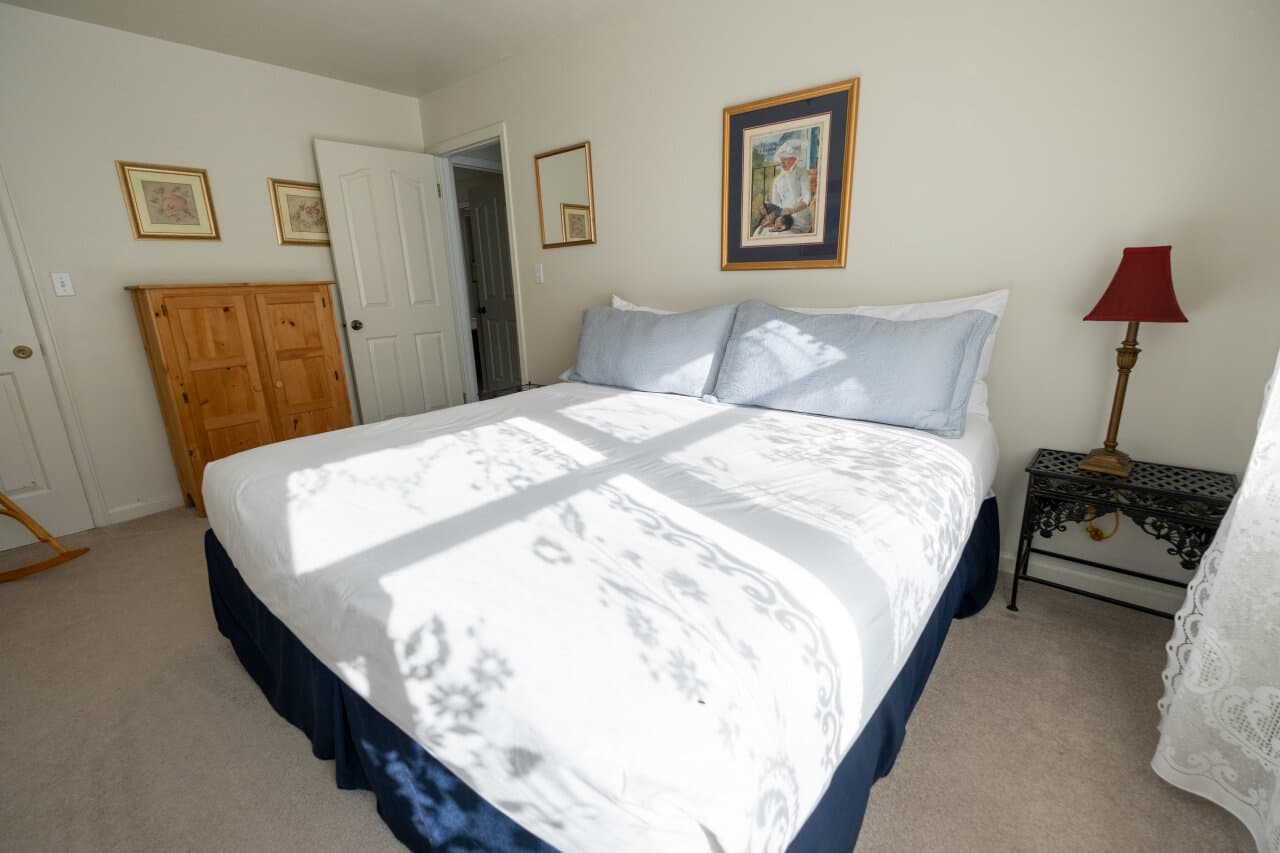 A cozy bedroom featuring a large bed with soft linens, a wooden dresser, and decorative wall art.