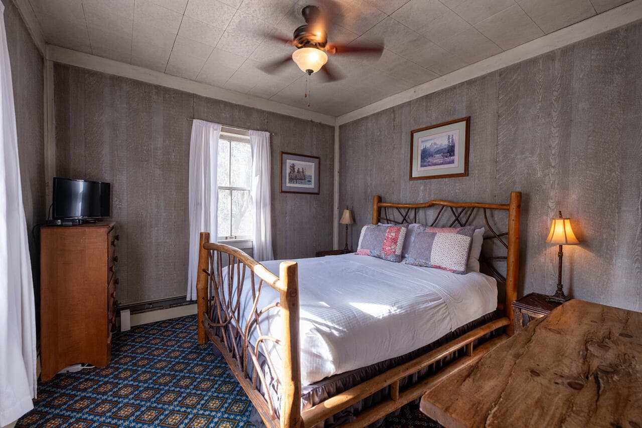 A cozy bedroom featuring a wooden bed, two windows, a dresser, and a small television.