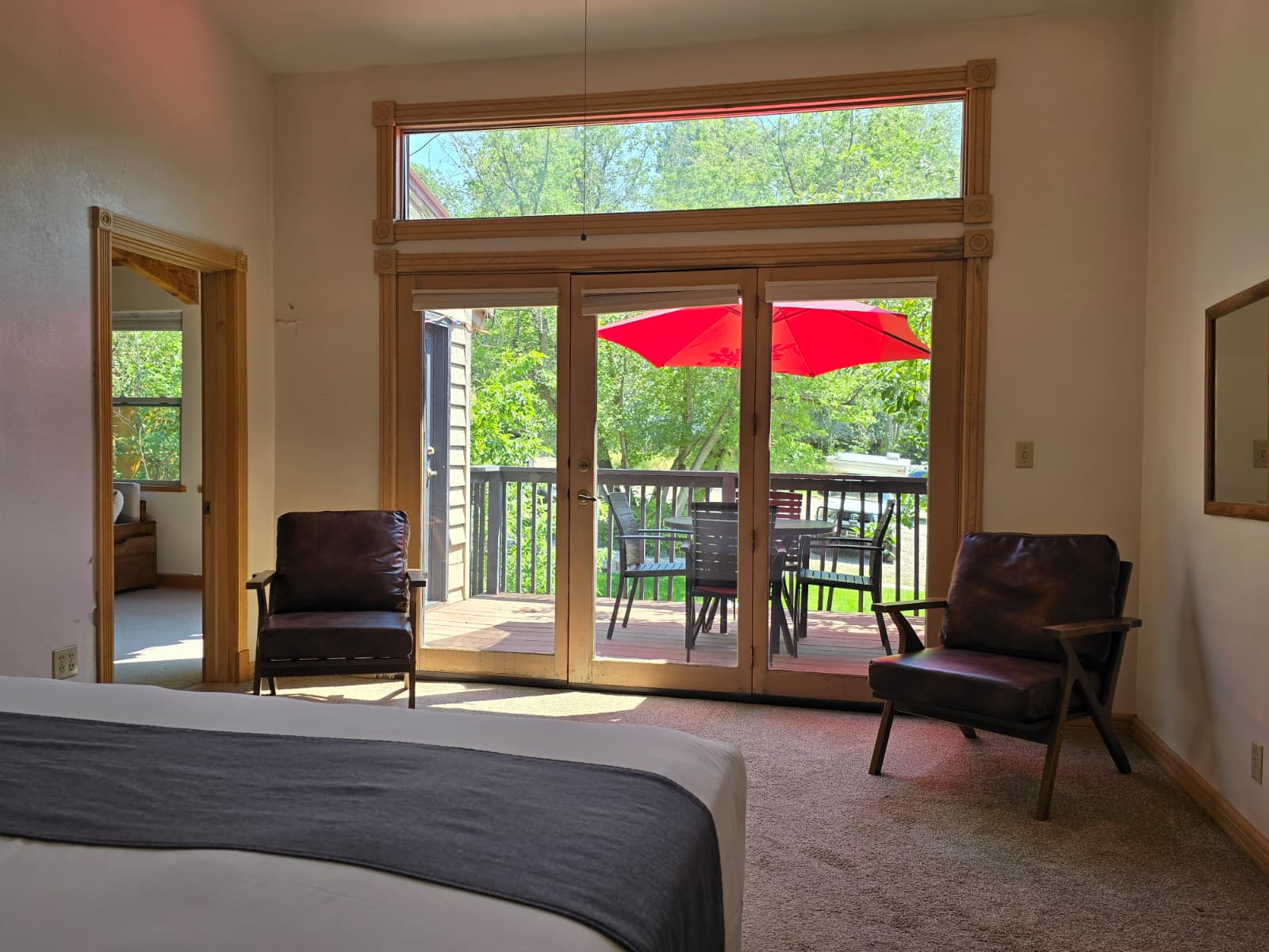 A cozy bedroom with two chairs, facing a patio door that opens to a deck with an umbrella.