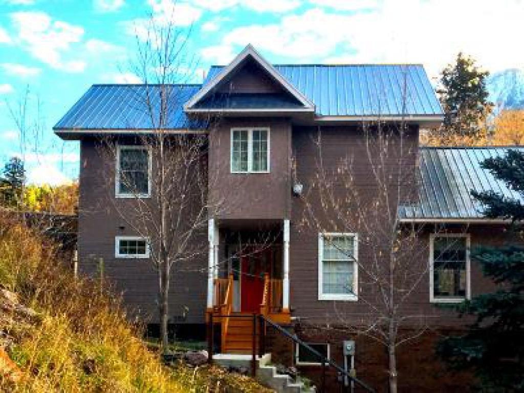 A modern two-story house with a metal roof, surrounded by sparse trees and grass.