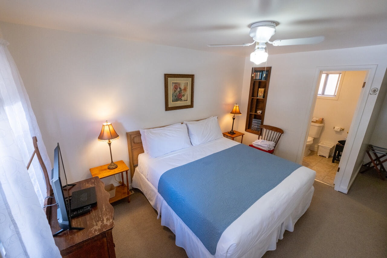 Cozy hotel room with a double bed, two lamps, a TV, and an adjoining bathroom.