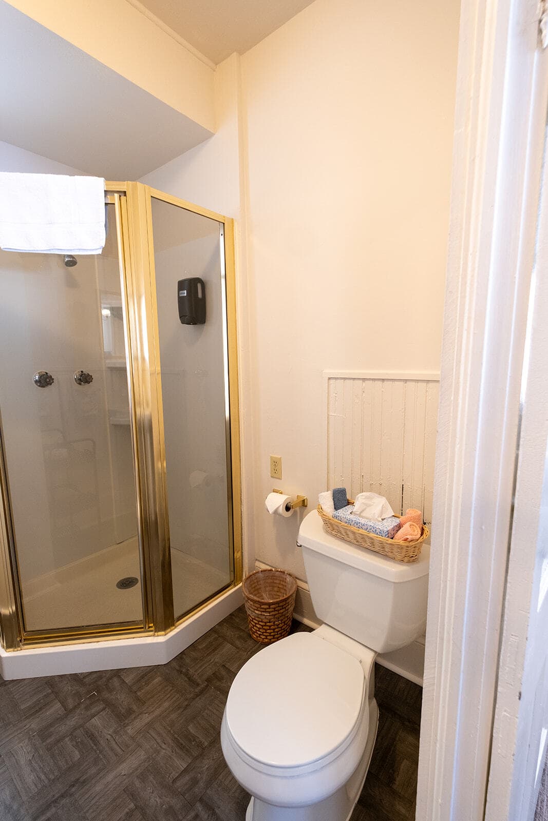 A small bathroom featuring a shower stall, toilet, and a basket of towels.
