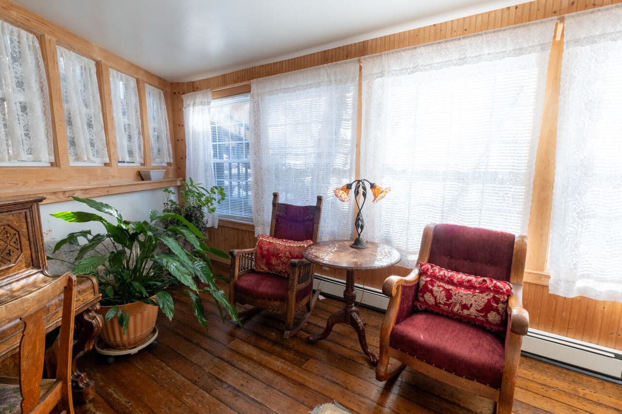 A cozy sunlit sitting area with two armchairs, a small table, and a potted plant.
