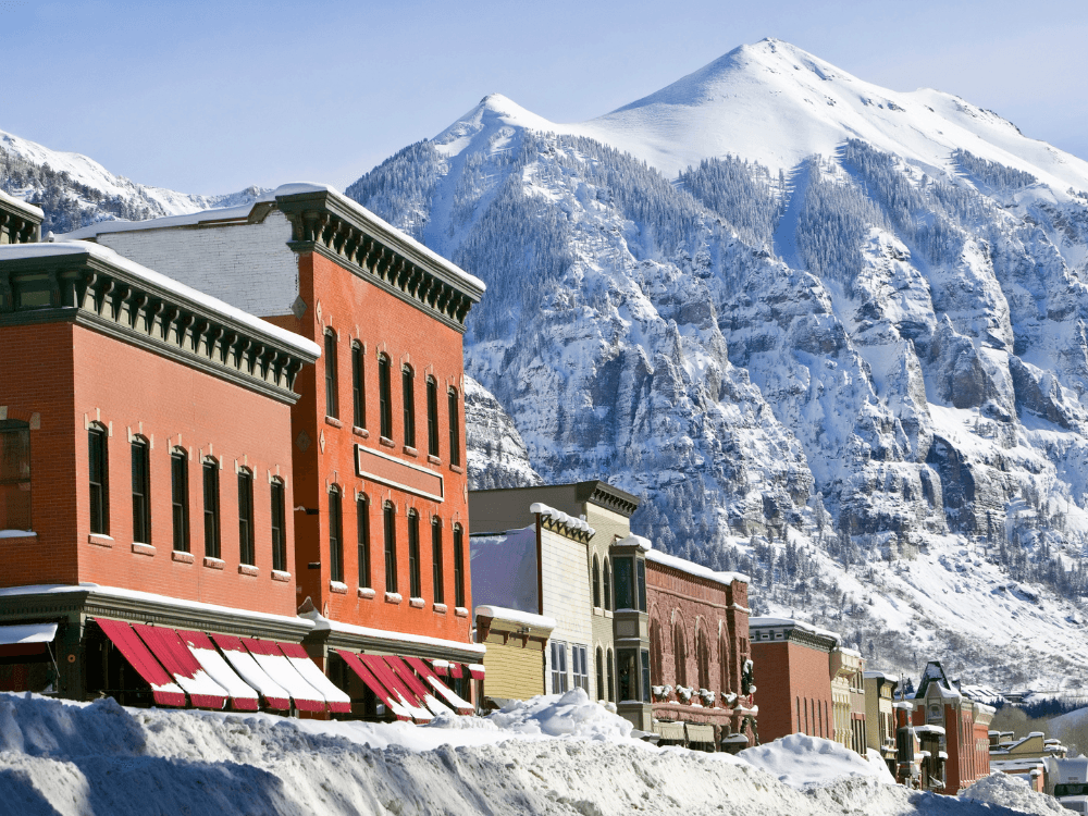 Snow-covered buildings with peaks of a mountain in the background.