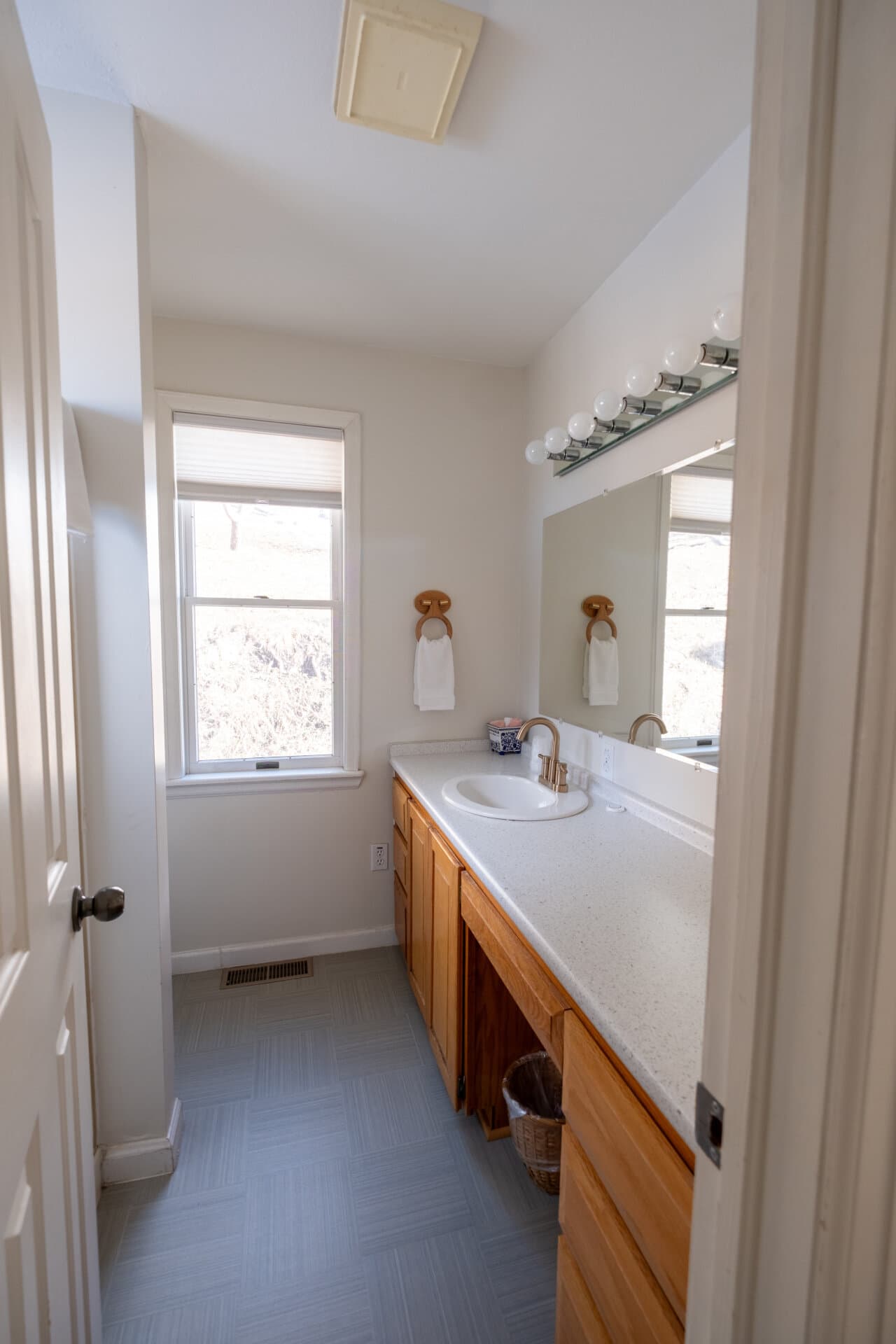 A spacious bathroom featuring a sink, wooden cabinetry, a mirror, and a window with natural light.