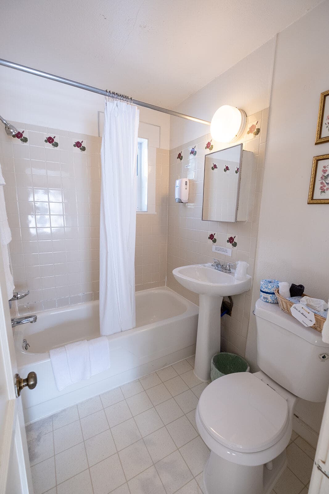 A small, bright bathroom featuring a bathtub, sink, toilet, and floral accents.