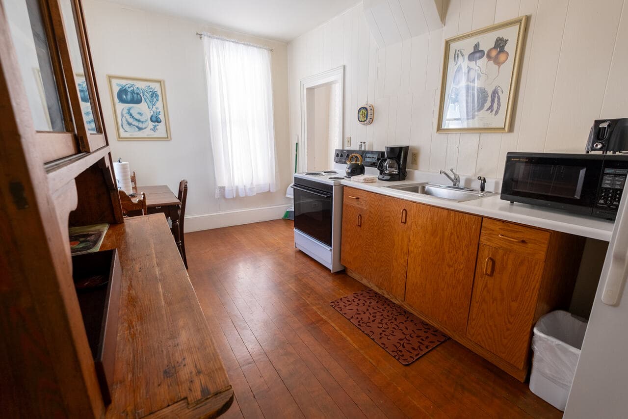 A cozy kitchen with wooden cabinets, a window letting in natural light, and various appliances including a stove and microwave.