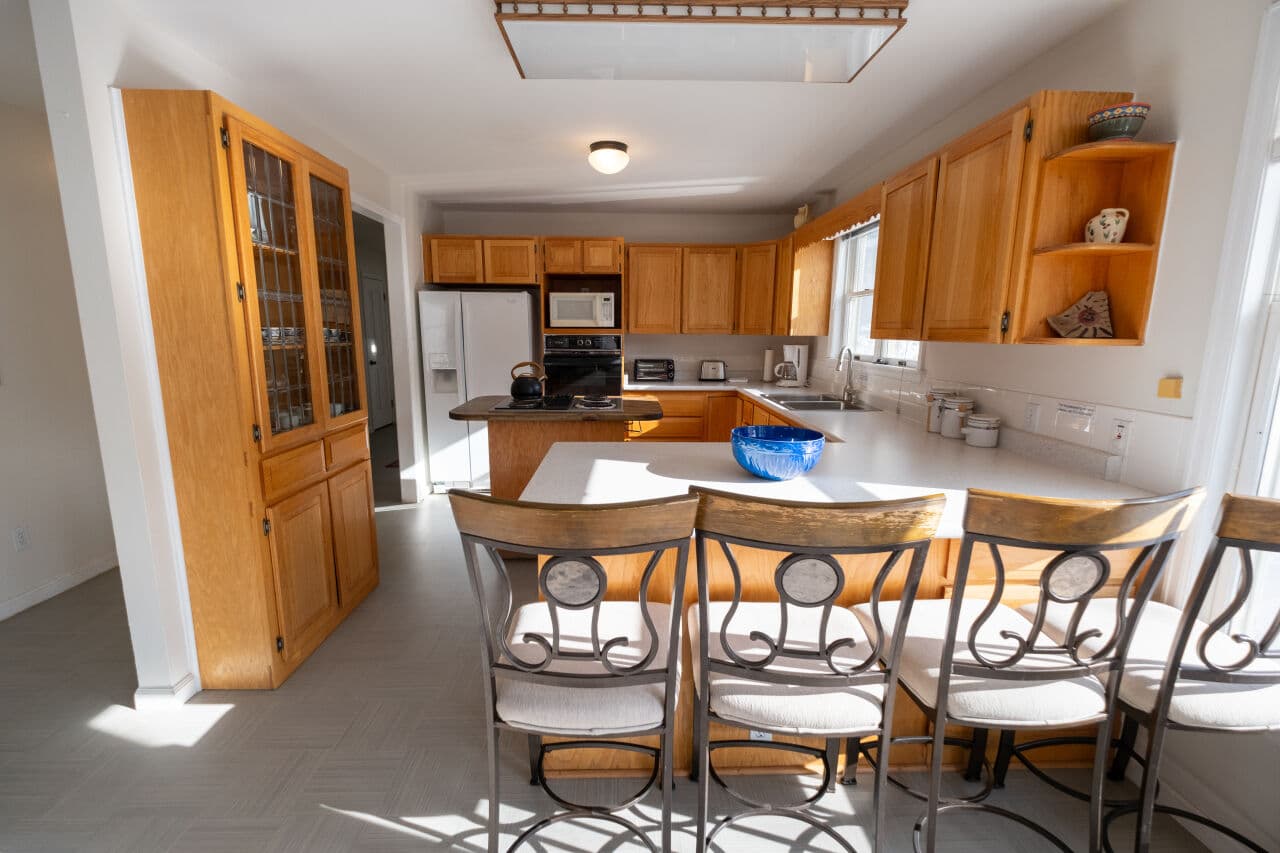 A bright, modern kitchen featuring wooden cabinets, stainless steel appliances, and a seating area with barstools.