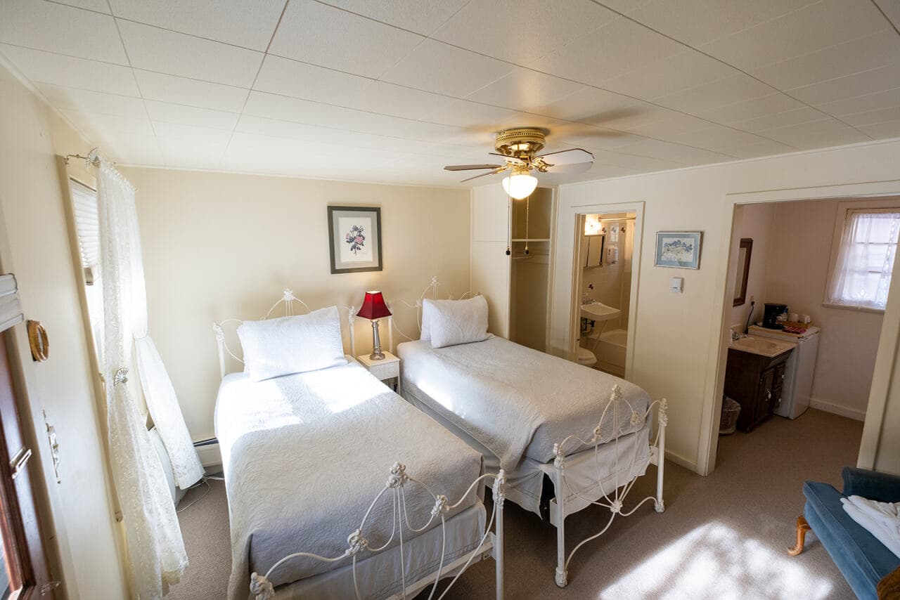 A cozy bedroom featuring two twin beds, a small table lamp, and an adjoining bathroom.