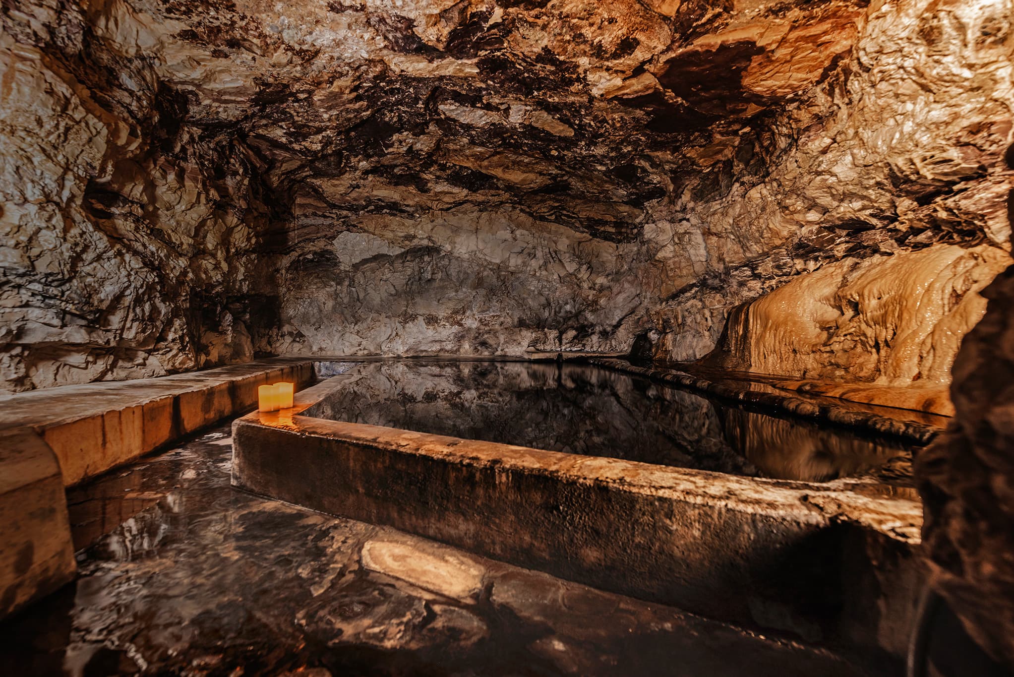 A dimly lit cave with a natural pool surrounded by rough stone walls.