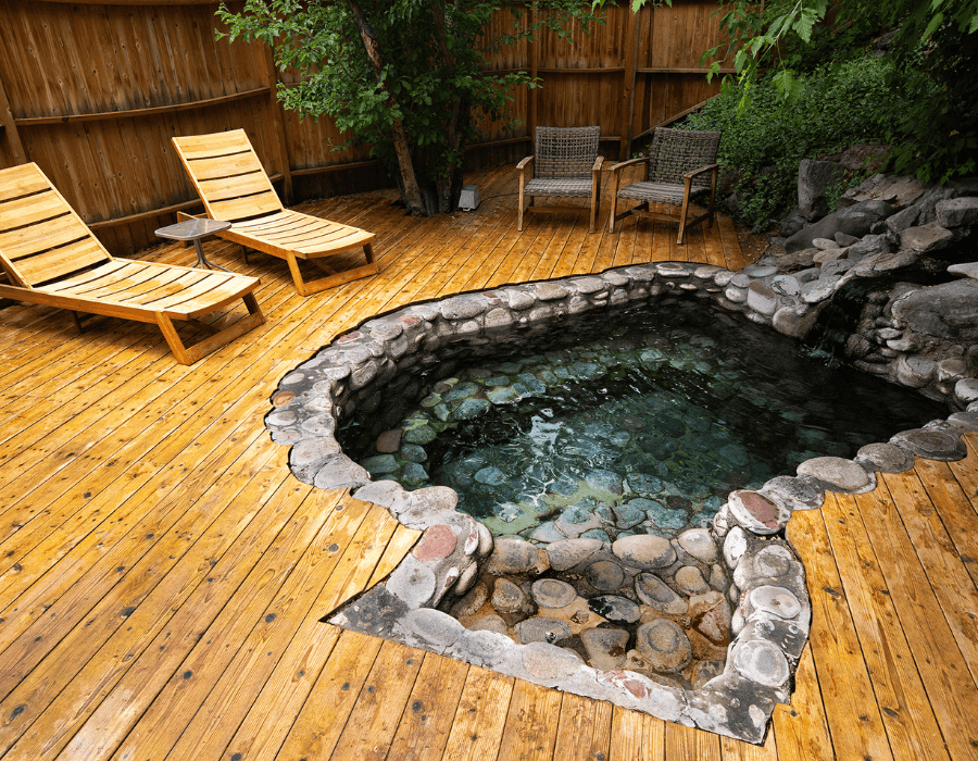 A wooden deck features two lounge chairs beside a natural stone hot tub.