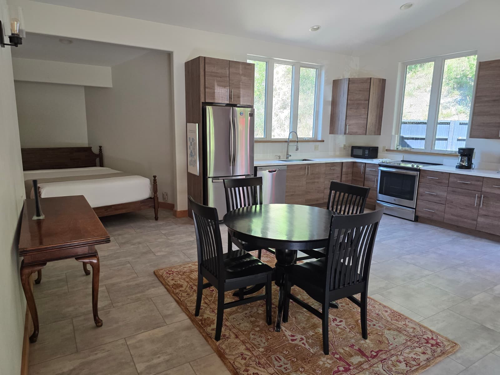 A modern, open kitchen and dining area with a round table, black chairs, and a bed visible in the background.