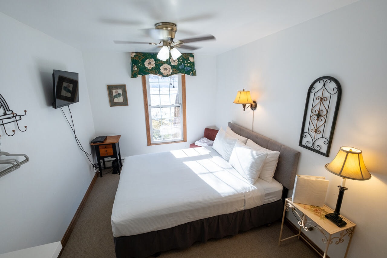 A cozy bedroom featuring a queen-sized bed, a window, and ambient lighting.
